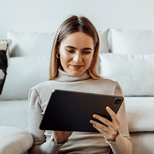 Woman smiling while using tablet with back up against couch