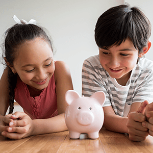 Two young kids laying on floor with piggy bank