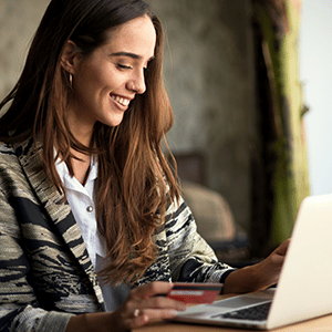 Woman smiling and holding credit card in hand while using computer